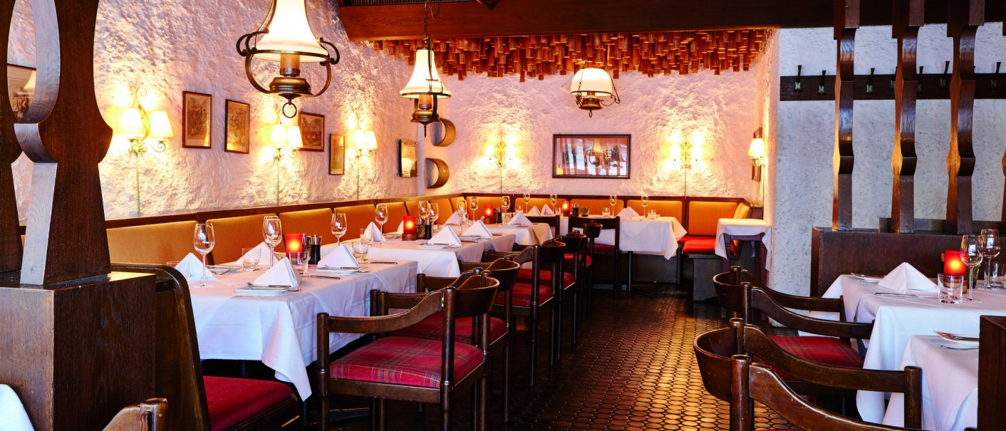 Cozy restaurant with wooden furniture, white tablecloths and warm lighting. The walls are rustic, decorated with pictures and lamps., © Steigenberger Graf Zeppelin Cozy restaurant with wooden furniture, white tablecloths and warm lighting. The walls are rustic, decorated with pictures and lamps., © Steigenberger Graf Zeppelin
