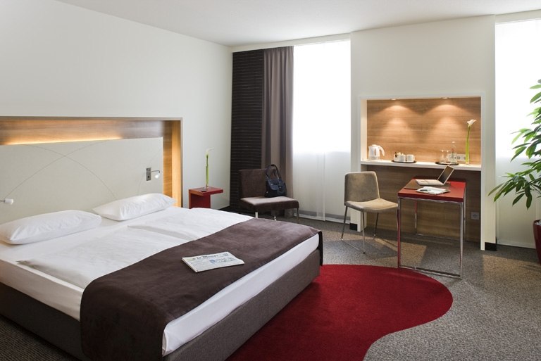 Modern hotel room with double bed, desk, chair and seating area. Light-colored walls, red carpet and plants create an inviting atmosphere., &copy; Mercure Stuttgart Airport Messe