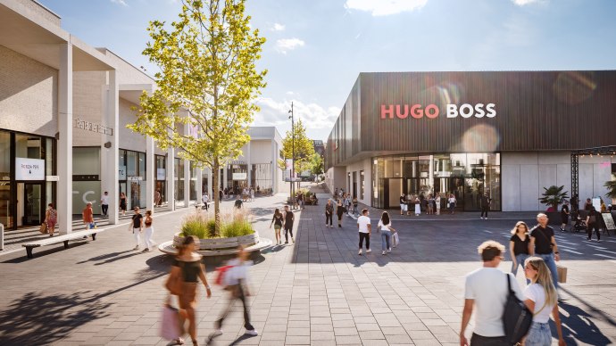 Menschen flanieren in der Outletcity Metzingen. Links Geschäfte wie Patrizia Pepe, rechts ein Hugo Boss Store. Sonniges Wetter, moderne Architektur., © OUTLETCITY AG
