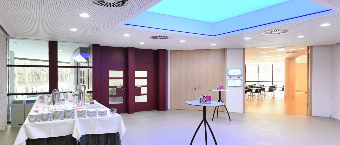 Modernes Foyer mit Tisch und Geschirr, helle Beleuchtung und Glastüren. Im Hintergrund ein Raum mit Tischen und Stühlen., © Guenter E. Bergmann - Photography